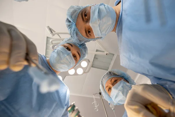 Confident surgeons looking down at camera while operating a patient. Idea of surgery and invasive treatments