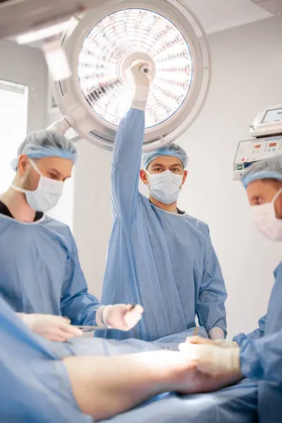 Три Уверенных Хирурга Выполняют Хирургическую Операцию Колене Пациента Операционной Концепция Лицензионные Стоковые Фото