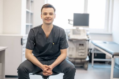 Klinikteki iş yerinde oturan ultrason teşhisinde uzman bir yetişkinin portresi. Ultrason muayenesi ve tanı konsepti