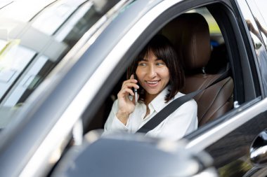 Arabada oturan ve telefonla konuşan güzel bir kadının portresi. İş aktarım hizmetleri, şoför portresi veya iş gezileri kavramı