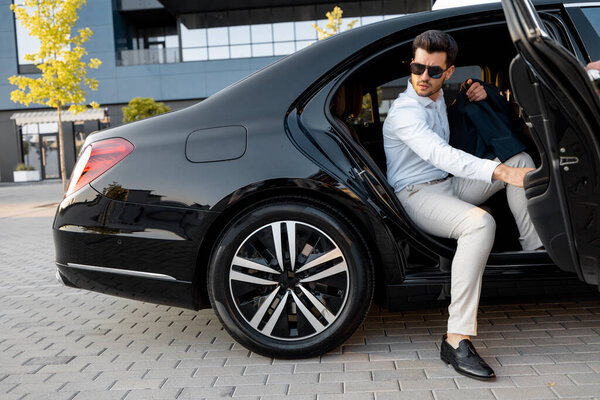 Portrait of elegant businessman gets out of a premium car. Transportation and business lifestyle concept