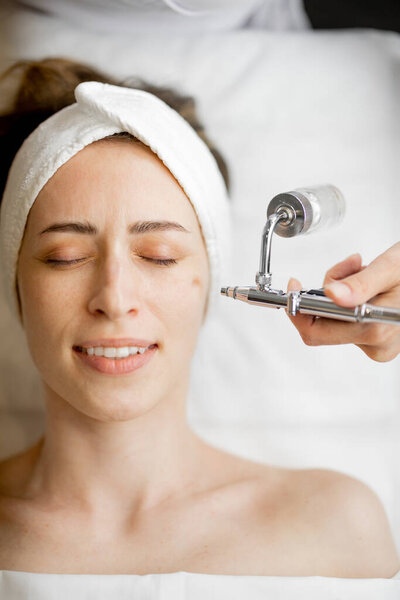 Young woman receiving oxygen mesotherapy on her face, close-up view from above. Concept of non-invasive and revitalizing skin treatment