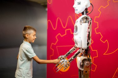 Küçük çocuk bilim müzesini gezerken insansı bir robotla el sıkışıyor. Modern teknoloji ve çocuk eğitimi kavramı