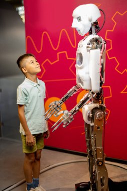 Küçük çocuk büyük bir heyecanla bilim müzesini ziyaret eden insansı robota bakıyor. Yeni teknoloji ve çocuk eğitimi kavramı
