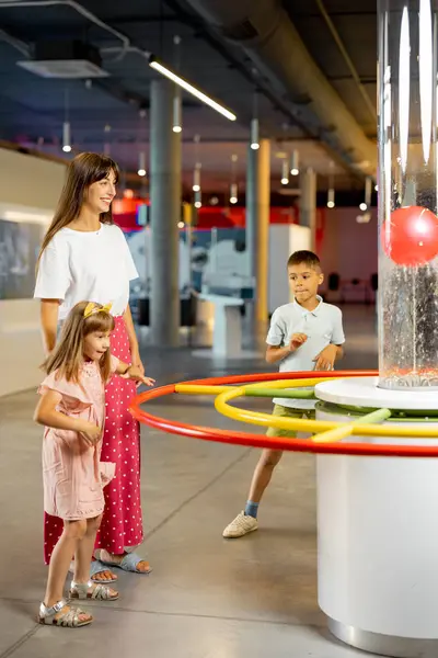 Mom with kids learn physics interactively on a model that shows physical phenomena while visiting a science museum. Concept of childrens entertainment and learning