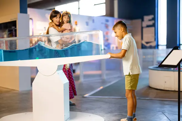 Mom with kids learn physics interactively on a model that shows physical phenomena while visiting a science museum. Concept of childrens entertainment and learning