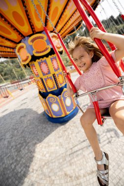 Çocuklar yaz tatili boyunca eğlence parkını ziyaret ederken atlıkarıncaya biniyorlar.