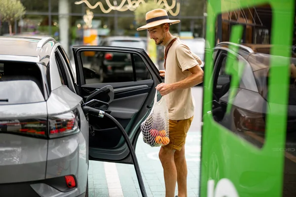 Man Met Boodschappen Wachten Voor Elektrische Auto Worden Opgeladen Het — Stockfoto