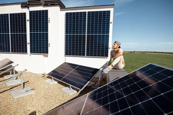 男人坐在他房子的屋顶上 上面有一个太阳能发电站 可再生能源和可持续性概念 — 图库照片