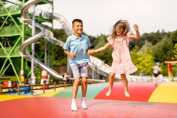 Çocuklar şişme trambolinde zıplıyor, yaz tatilinde lunaparkı ziyaret ederek eğleniyorlar. Kardeşi ve kız kardeşi birlikte vakit geçiriyorlar.