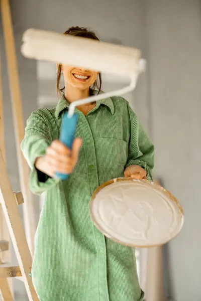 家の修理中にペイントローラーで立っている若い喜びとかわいい女性の肖像画 インテリアをリノベーションしながらハッピーレジャータイムのコンセプト ストック画像