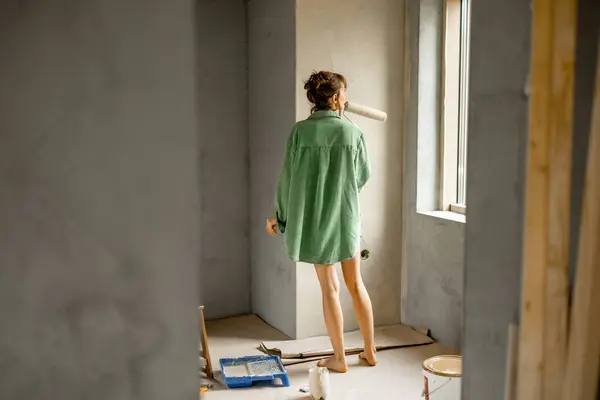 Junge Frau Streicht Wände Während Sie Ein Neues Haus Repariert lizenzfreie Stockfotos