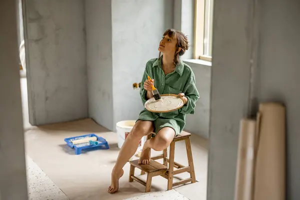 Młoda Kobieta Maluje Ściany Podczas Remontu Nowego Mieszkania Siedząc Krześle Obrazy Stockowe bez tantiem