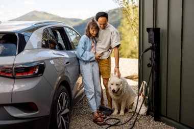 Evlerinin yanında sevimli beyaz köpekleri ve modern elektrikli arabaları olan genç bir çiftin portresi. Aile ve refah kavramı