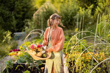 Gün batımında çiçek açan bir bahçede elinde bir sepet taze koparılmış çiçek tutan genç bir kadın. Doğayla mükemmel bir uyum anı.