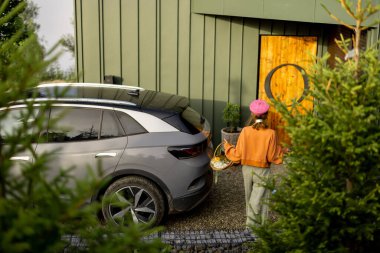 Çağdaş bir sığınağa barışçıl bir şekilde dönüşünü simgeleyen, eşsiz dairesel ahşap bir kapısı olan ve elinde bir sepet çiçekle modern bir eve yaklaşan bir kadın görülüyor.