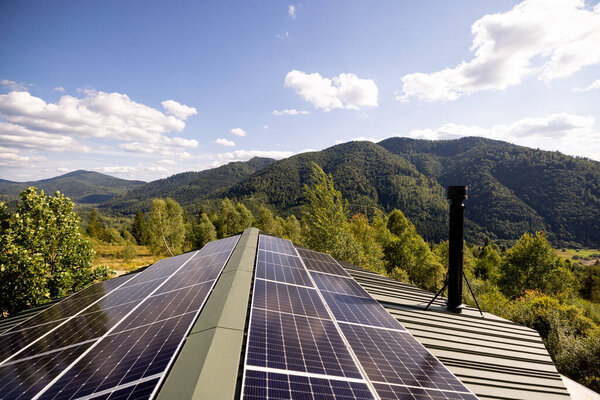 Solar panels installed on a rooftop with a stunning view of lush green mountains under a bright blue sky. A perfect blend of sustainable energy and natural beauty