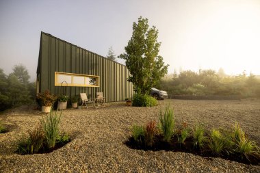 Modern bir kulübe, sakin bir doğal manzarayla çevrili, yumuşak sabah ışığında güneşleniyor. Doğaya barışçıl bir kaçış için mükemmel bir yer.