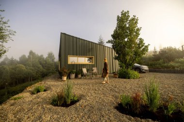 Modern bir kulübenin dışında huzurlu bir sabah ışığının tadını çıkaran bir insan, doğadaki sükunet ve yalnızlığın özünü yakalar.