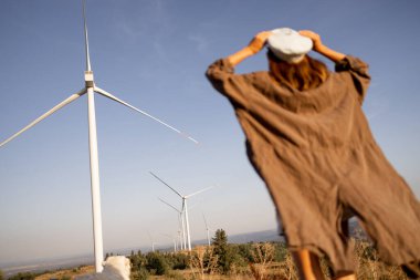 Person with outstretched arms embracing the power of wind energy, standing in front of large wind turbines, symbolizing renewable energy and sustainability clipart