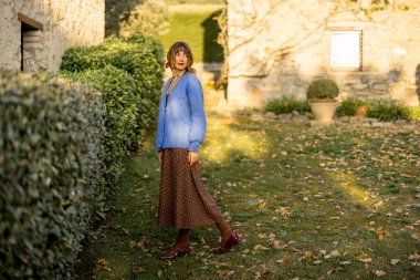 İki köpeği olan neşeli bir kadın güneşli bir kırsalda, taştan bir evin yanında oturuyor. Arkadaşlığın, kırsal çekiciliğin ve neşenin mükemmel bir tasviri. 