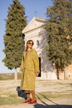 Toskana kırsalında tarihi bir kilisenin yanında duran zarif bir kadın sonsuz bir cazibe ve tarz yayıyor. Mükemmel bir miras, kırsal dinginlik ve modaya uygun yaşam manzarası.