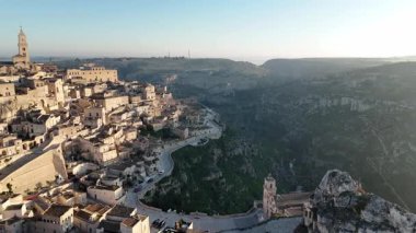 Güneşin doğuşuyla birlikte antik Matera şehrinin engebeli uçurumlara kurulmuş tarihi taş binalarıyla nefes kesici hava aracı görüntüsü.