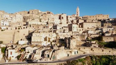 Matera Katedrali 'nin hava aracı görüntüsü antik şehir manzarasının üzerinde yükseliyor. Tarihi kasabanın merkezinde geleneksel taş konutlar ve ortaçağ mimarisi sergileniyor.