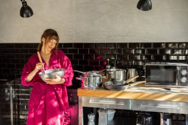 Huzurlu bir evde karışımı karıştıran bir kadın, mutfakta sakin bir sabahın tadını çıkarıyor. Sahne, ev yapımı yiyeceklerin sıcaklığını, farkındalığı ve basit yaşam tarzını somutlaştırıyor.