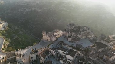 Basilica Cattedrale di Matera 'nın ve Matera, İtalya' daki antik taş konutların hava aracı görüntüsü. Engebeli tepelere oyulmuş tarihi manzara ortaçağ şehirlerini vurguluyor.