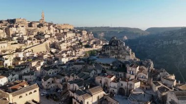 Güneşin doğuşuyla birlikte antik Matera şehrinin engebeli uçurumlara kurulmuş tarihi taş binalarıyla nefes kesici hava aracı görüntüsü.