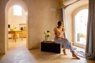 Geleneksel bir Matera evinde bir kadın güneş ışığında çıplak ayakla oturuyor. Bu resim sakin, düşünceli bir yaşam yayar ve yaşam tarzı, iç mekan veya sağlıklı odaklı yaratıcı kullanım için idealdir.