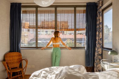 Bir kadın pencerenin kenarında duruyor sabah ışığında yıkanmış, sakin ve gün ışığıyla dolu Roma 'daki evinde yeni bir günü kucaklıyor.