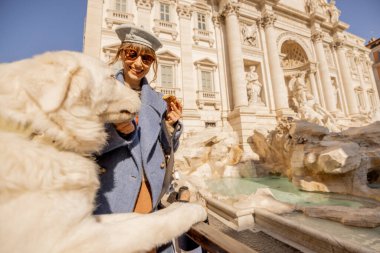 Neşeli bir kadın, Trevi Çeşmesi 'nin önünde tüylü beyaz köpeğiyle bir parça cannolo paylaşır ve Roma' da yürek ısıtan bir yolculuk anını yakalar.
