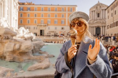 Şık bir kadın Roma ikonik Trevi Çeşmesi 'nin önünde dondurmayı seviyor, hareketli meydanın güneş ışığını ve hareketli atmosferini emiyor.