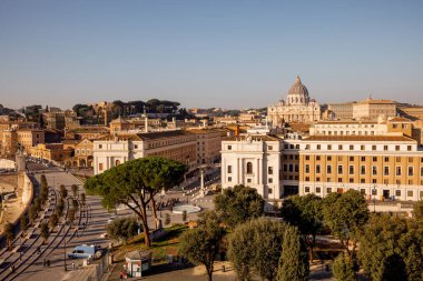 Castel Sant Angelo 'dan Vatikan Şehri ve St. Peters Bazilikası üzerinde geniş çaplı bir manzara, tarihi binalar ve Roma çam ağaçlarıyla çevrili Via della Conciliazione' nin planını ele geçiriyor.