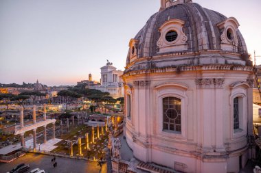Günbatımında parlayan tarihi bir kubbe ve antik Roma kalıntılarının manzarası. İkonik Altare della Patria, Roma akşam siluetinin üzerinde yükseliyor.