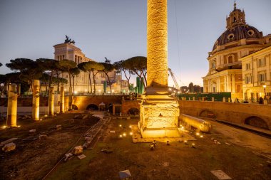 Roma 'nın ikonik Trajans Sütunu ve Altare della Patria' nın akşam manzarası, alacakaranlık gökyüzüne karşı aydınlandı, harabeler, kiliseler ve kaldırım taşı sokaklarla çevrili.