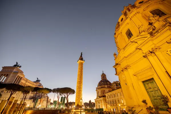 Roma 'nın ikonik Trajans Sütunu ve Altare della Patria' nın akşam manzarası, alacakaranlık gökyüzüne karşı aydınlandı, harabeler, kiliseler ve kaldırım taşı sokaklarla çevrili.
