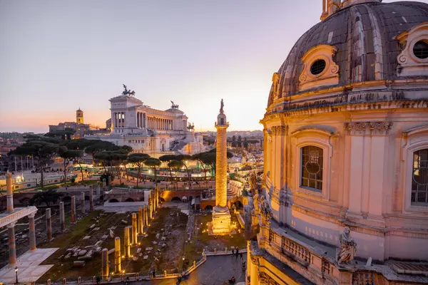 Günbatımında parlayan tarihi bir kubbe ve antik Roma kalıntılarının manzarası. İkonik Altare della Patria, Roma akşam siluetinin üzerinde yükseliyor.