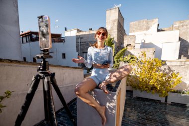 Neşeli bir kadın kendini güneşin altındaki bir çatıda kaydediyor. Etkilenen yaşam tarzı, dijital göçebeler, uzaktan çalışma veya sosyal medya pazarlaması gibi konular için harika