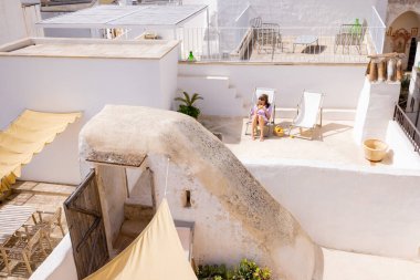 Akdeniz dokuları, yumuşak ışık ve kırsal güney İtalya cazibesiyle çevrili, limon ve şezlongla bembeyaz bir terasta dinlenen bir kadın.
