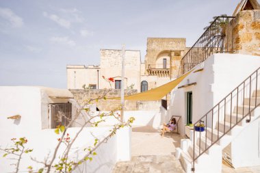 Çatı katındaki terasta bir kitapla rahatlayan, yelken tepe örtüsüyle gölgelenen, beyazlatılmış duvarlar ve Akdeniz mimarisi yaz kaçışıyla çevrili bir kadın.