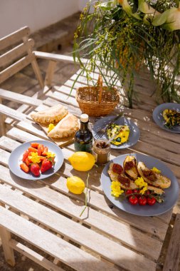 Taze meyve, limon, bruschetta ve zeytinyağlı ahşap bir masada canlı Akdeniz brunch 'ı. Doğal ışık ve rahat açık hava atmosferiyle kırsal yaz manzarası