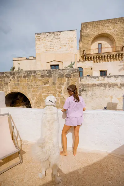 Bir kadın ve beyaz köpeği güneşli bir çatıda sakin bir sabah geçirdiler. Tarihi taş binalar ve güney İtalya 'da bir palmiye ağacı vardı.