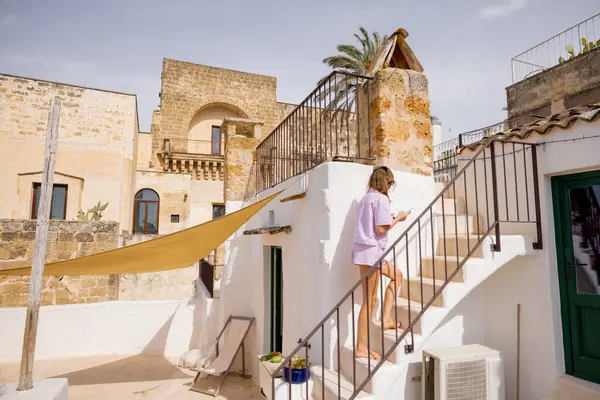 Pastel giysili bir kadın, güneşle yıkanmış taş duvarlar ve Akdeniz mimarisi ile çevrili çatıdaki merdivenleri tırmanıyor büyüleyici bir İtalyan kasabasında sakin bir an.