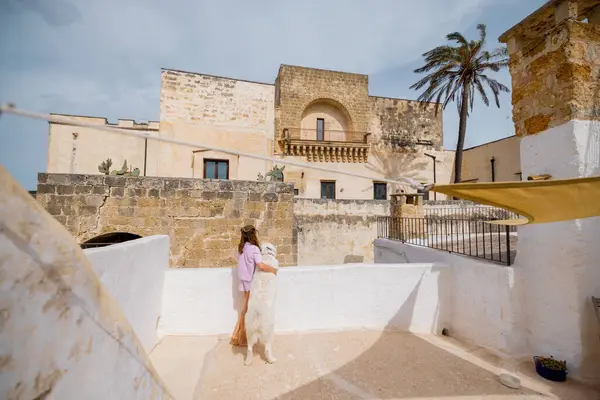 Bir kadın ve beyaz köpeği güneşli bir çatıda sakin bir sabah geçirdiler. Tarihi taş binalar ve güney İtalya 'da bir palmiye ağacı vardı.