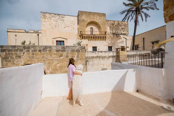 Bir kadın ve beyaz köpeği güneşli bir çatıda sakin bir sabah geçirdiler. Tarihi taş binalar ve güney İtalya 'da bir palmiye ağacı vardı.