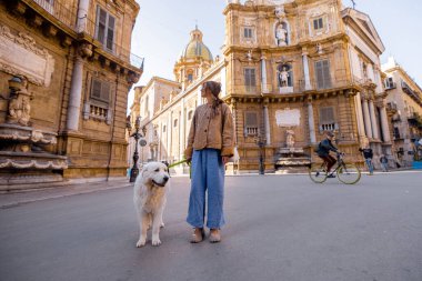 İtalya 'nın Palermo kentindeki Quattro Canti meydanında büyük beyaz köpeğini gezdiren bir kadın. Görüntü yavaş turizmi, evcil hayvanlarla bağlantıyı ve sakin şehir keşfini seyahat için mükemmel kılıyor, evcil hayvan