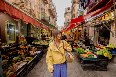 Sarı ceketli bir kadın Sicilya 'da canlı bir yerel markette geziniyor, taze ürünlerle çevrili. Görüntü otantik seyahat, kültürel dalma ve yavaş yaşam tarzını aktarıyor. 